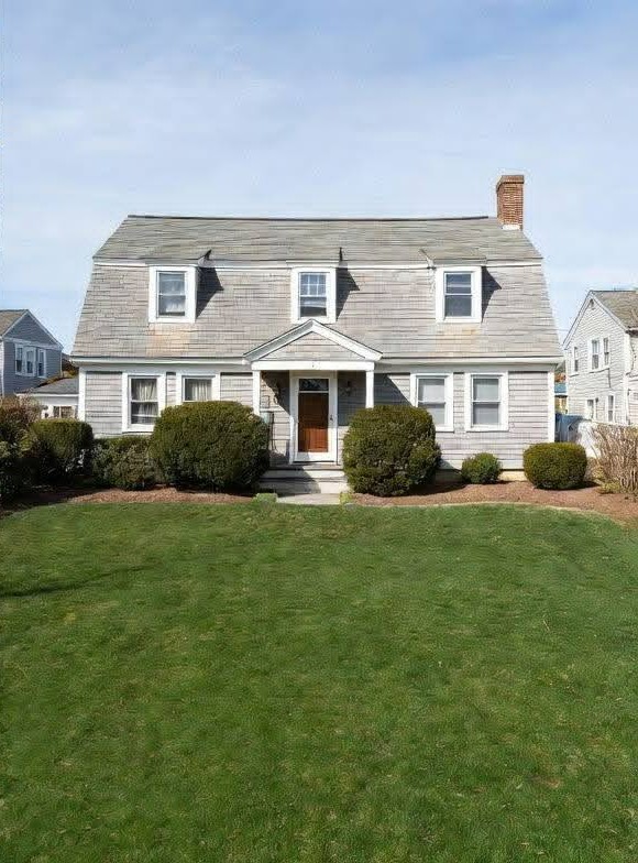 A lush, freshly cut green lawn in front of a gray gambrel-roofed home under a bright blue sky